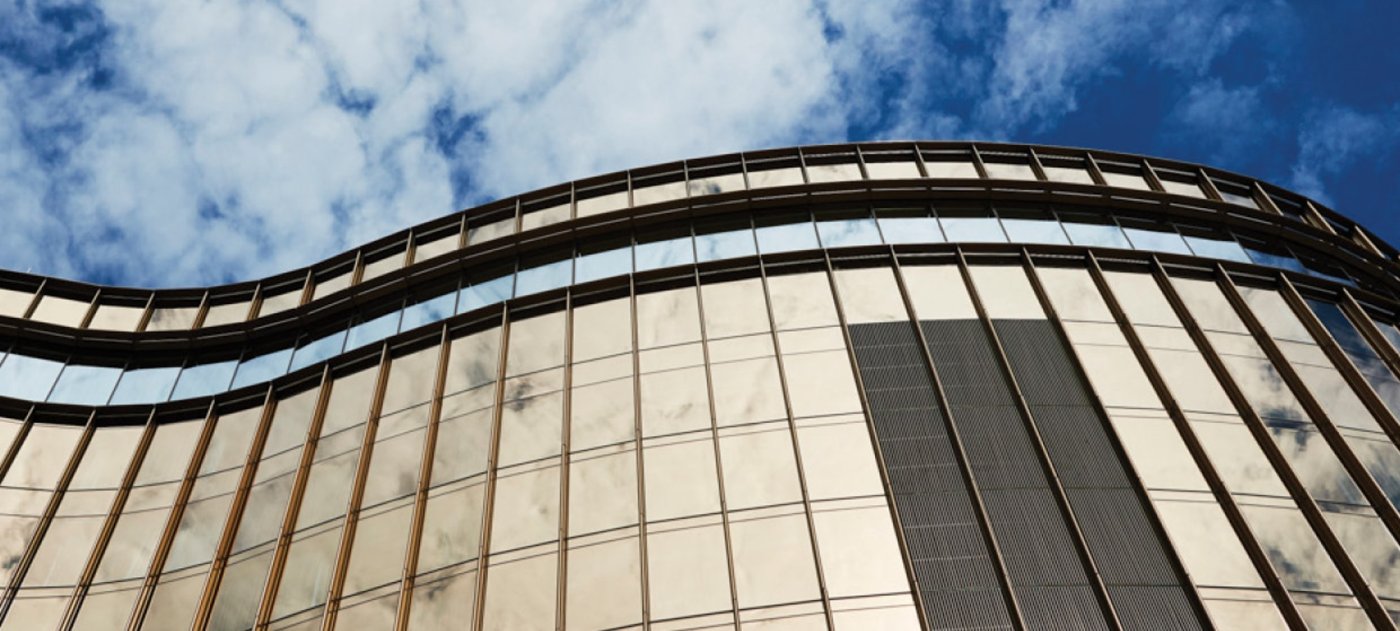 The hot spots are not only the vision glass. Horizontal canopy glazing and metal cladding both reflect, and a slanted or curved surface can be worse than a flat one.