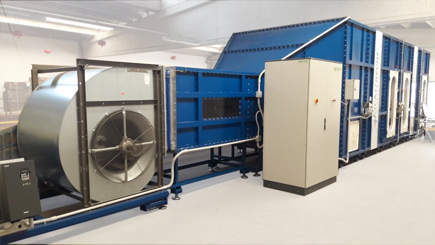 A large fan unit and ducting in a laboratory hall, facing a blue test frame