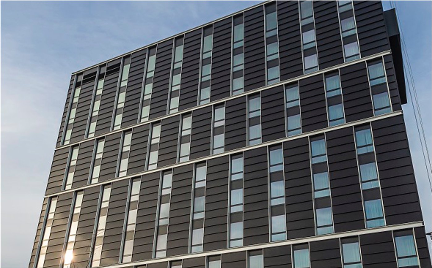 Generation moved onto the wall. Where a new building has to supply a set share of its energy on site, a tall one has almost no roof with which to do it, and the façade becomes the only surface large enough.