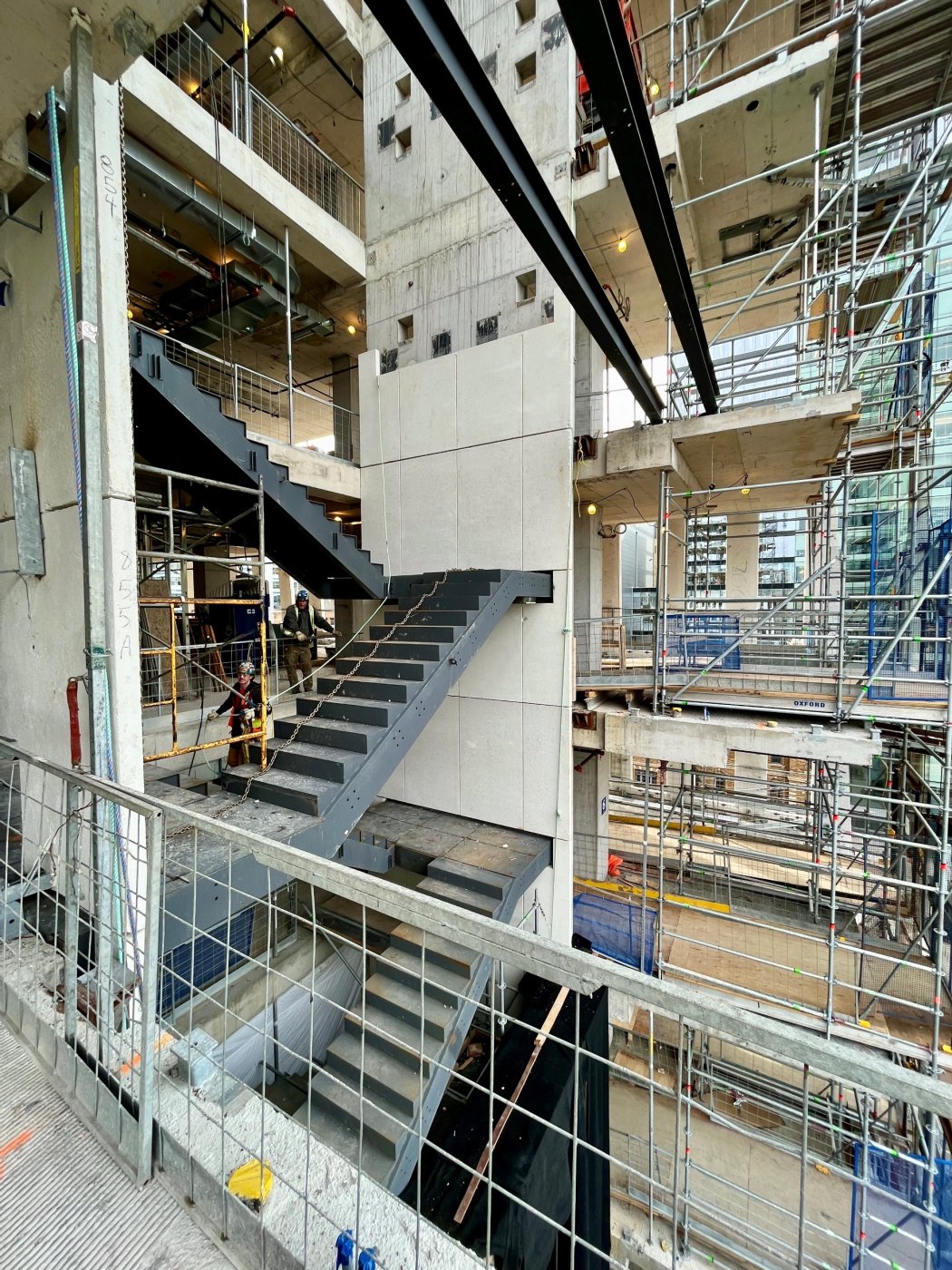 The stair, expressed. Normally buried in a core, the exit stair becomes the reveal on the corner, in fire-rated glazing so daylight reaches the shared corridors.
