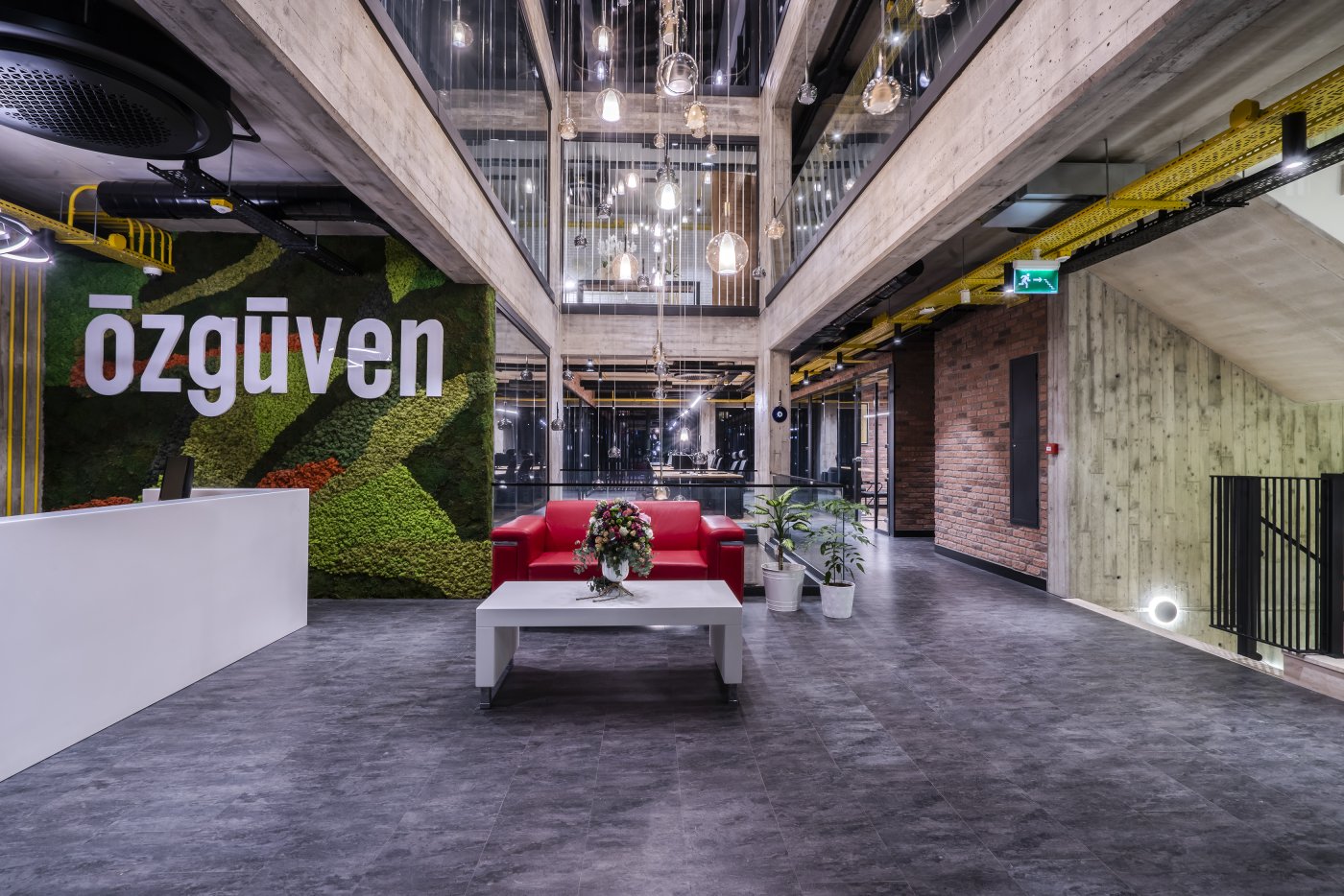 An office reception under exposed services, with the practice name on a planted wall