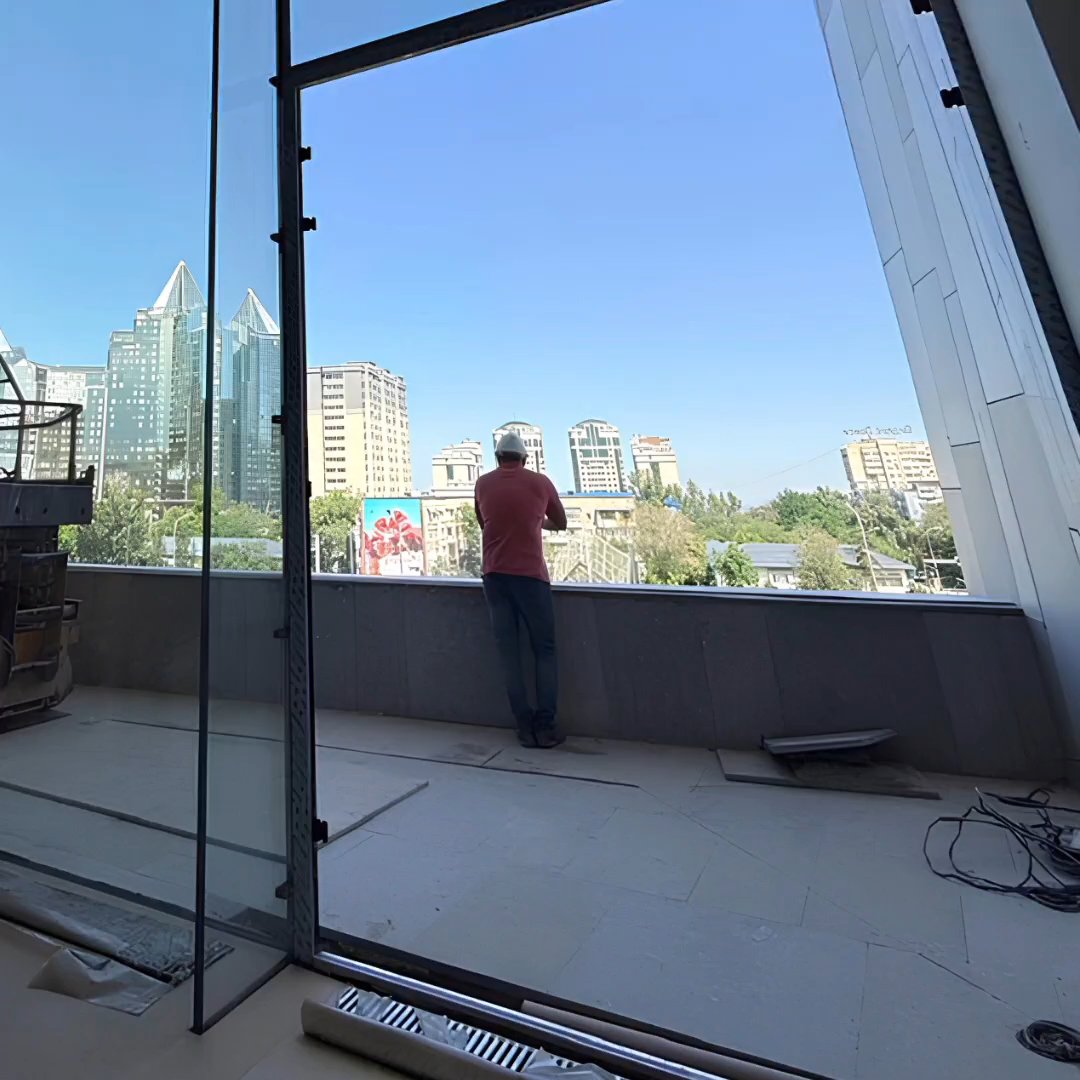 A man leaning on a frameless glass balustrade on an unfinished terrace above a city