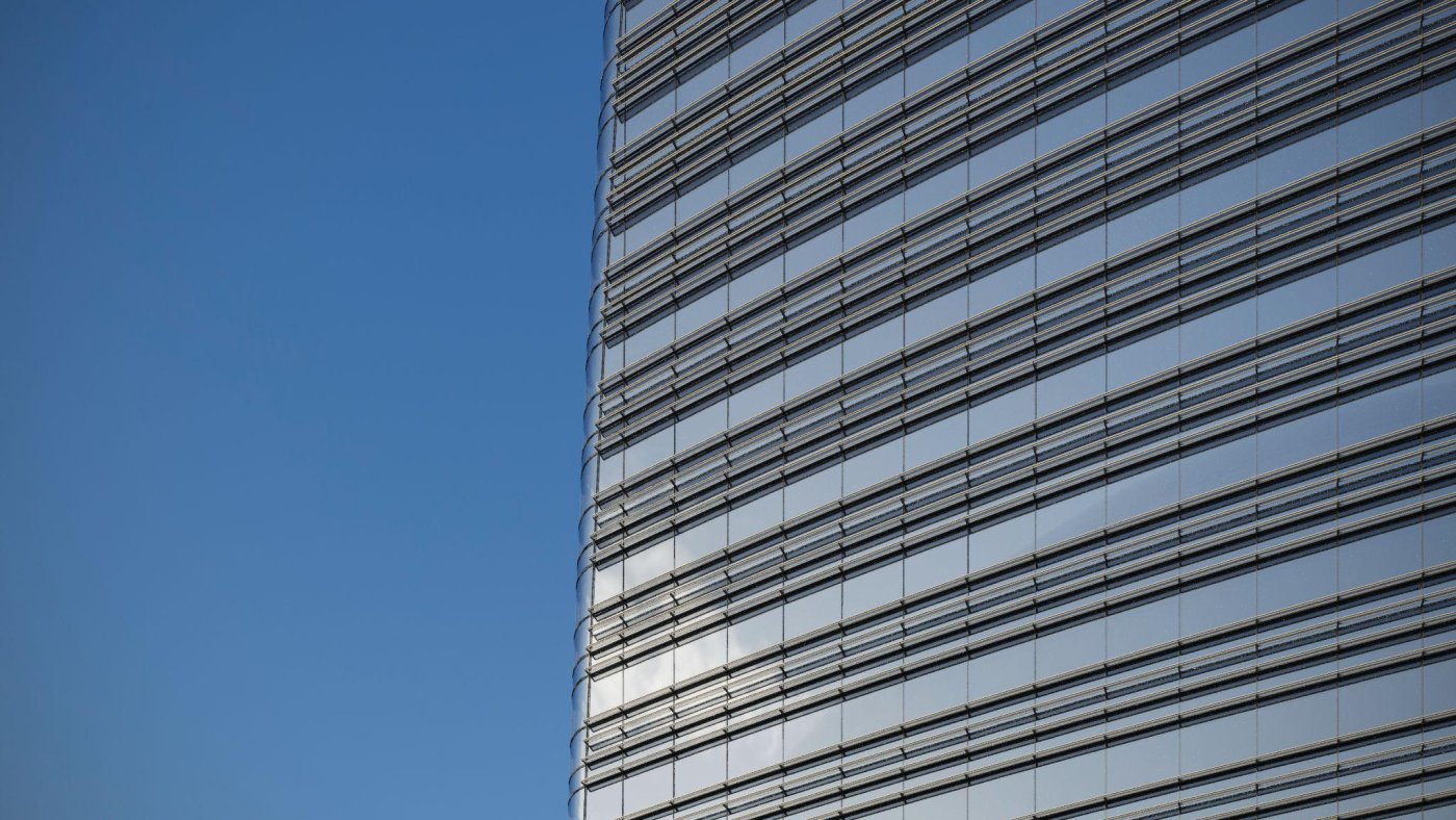 Two fins that shade and generate. The photovoltaics in the fins are estimated at 160,000 kilowatt hours a year, and the structure holding them was cut to the minimum that survives a typhoon so the panels can repay themselves.