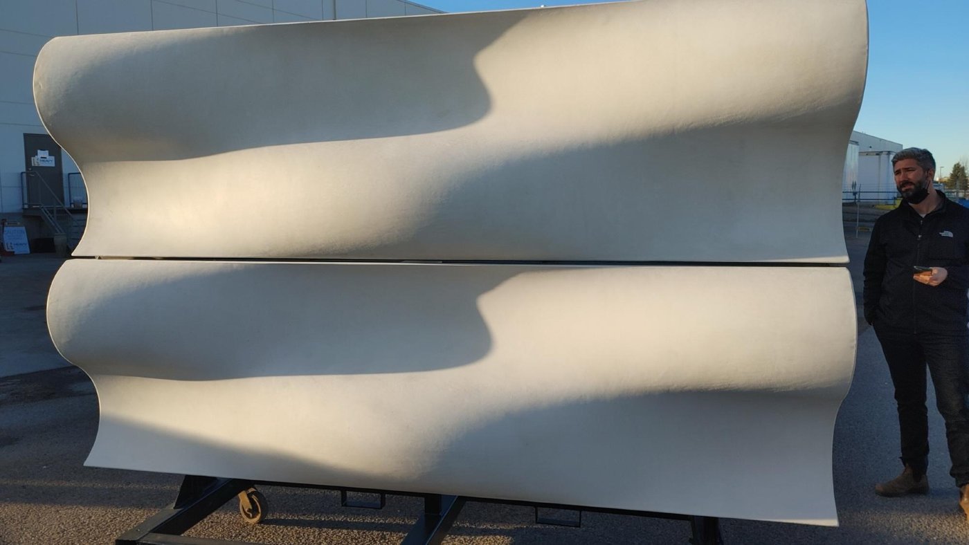 A large undulating glass-fibre-reinforced concrete wall with two people for scale