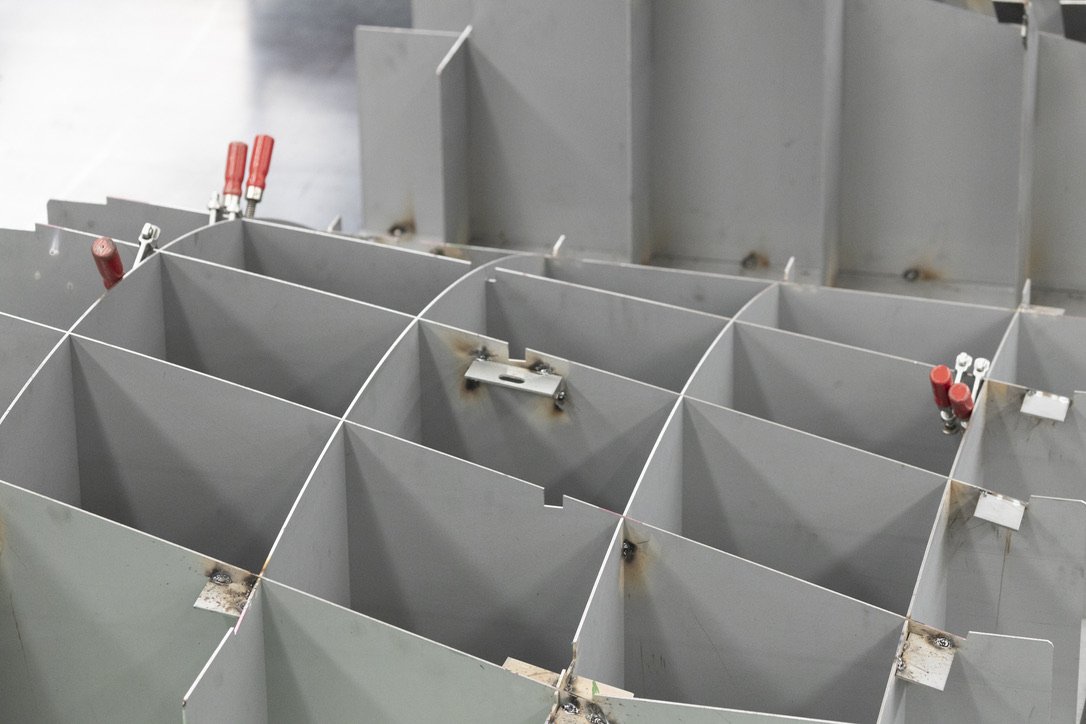 A wing, not a casting. The bench borrows aircraft construction, a waffle grid of flat plates that will take almost any shape, skinned over in four millimetre aluminium sheet.