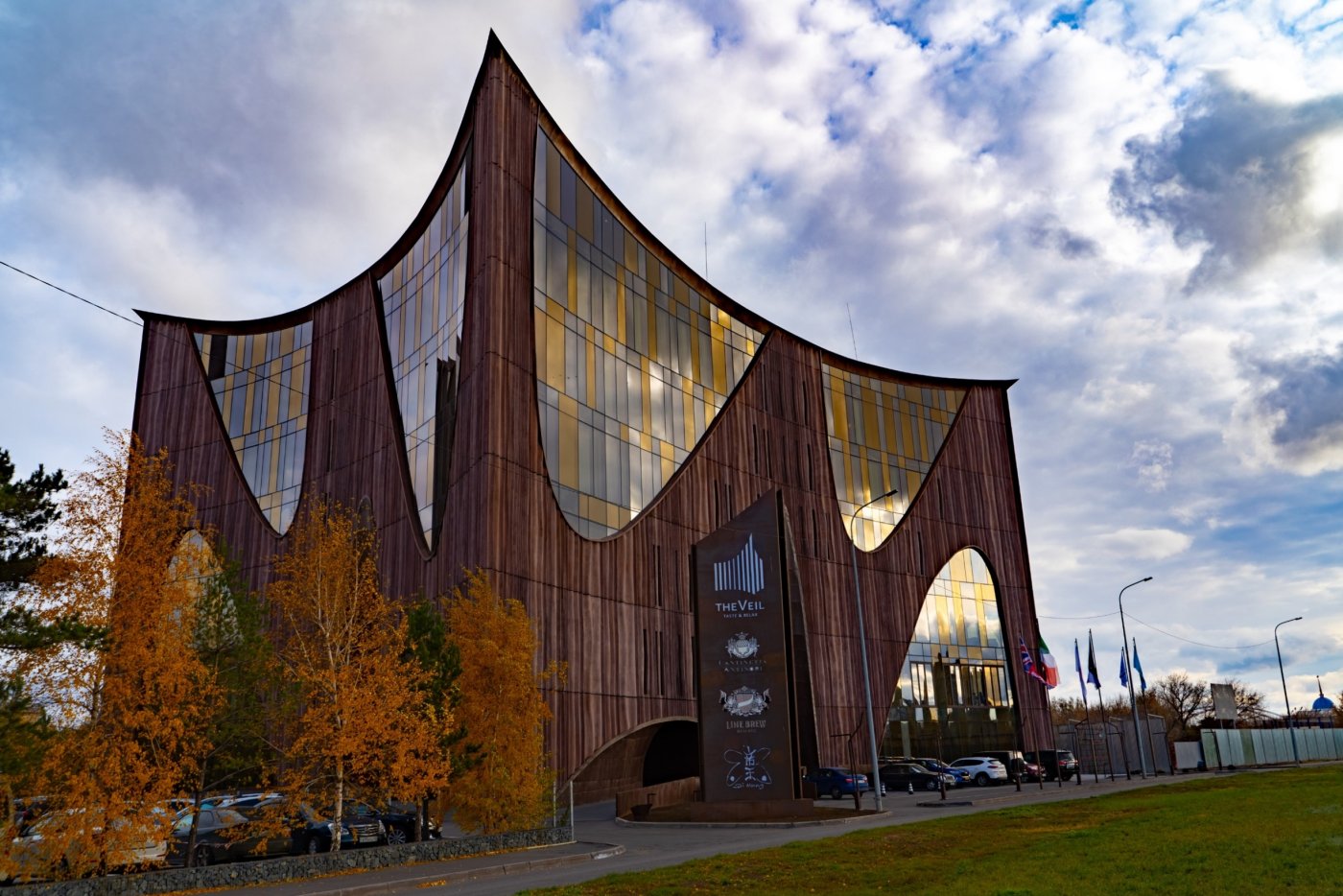 A building with sweeping copper-toned surfaces and tall glazed openings in warm amber tints