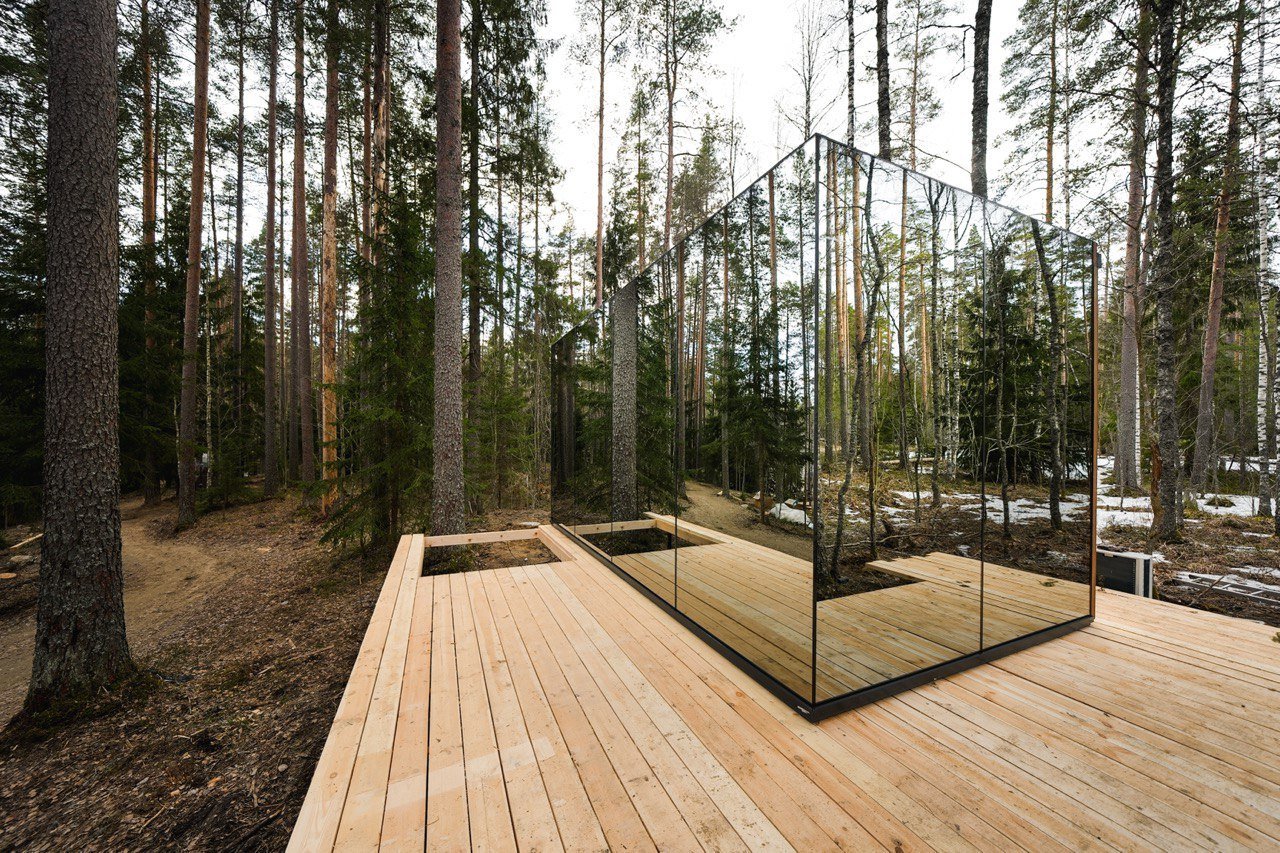 A mirrored glass volume standing among pines, its faces reflecting the trees around it