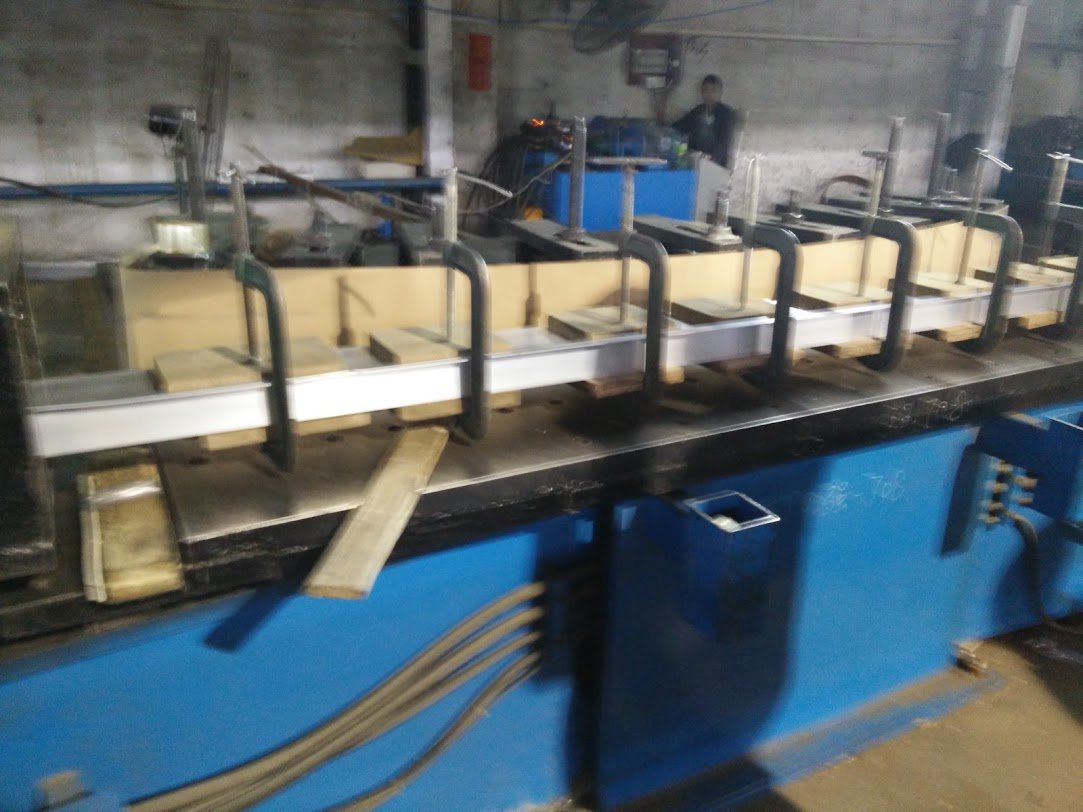 Stretch forming the profiles. With a 200 mm deep section on a 260 m building, three-roller bending was ruled out; profiles were pulled from each side against a standardised mould and clamped.