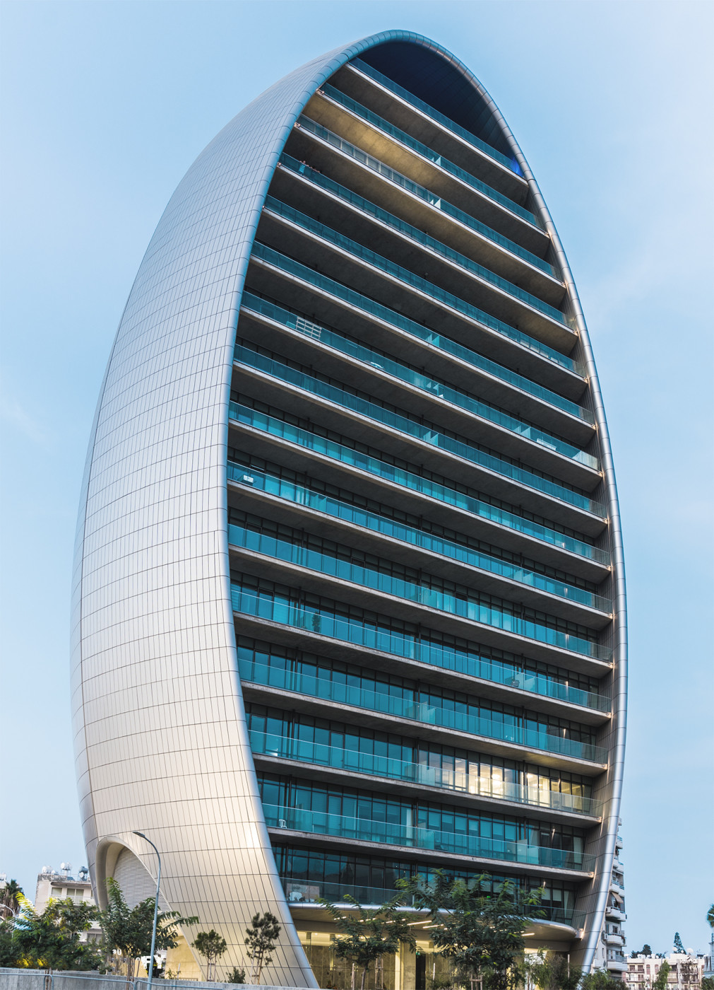The Oval, Limassol. A rounded form that came out of solar exposure rather than styling, with deep balconies on the south face doing the shading so the glass can stay fully transparent.